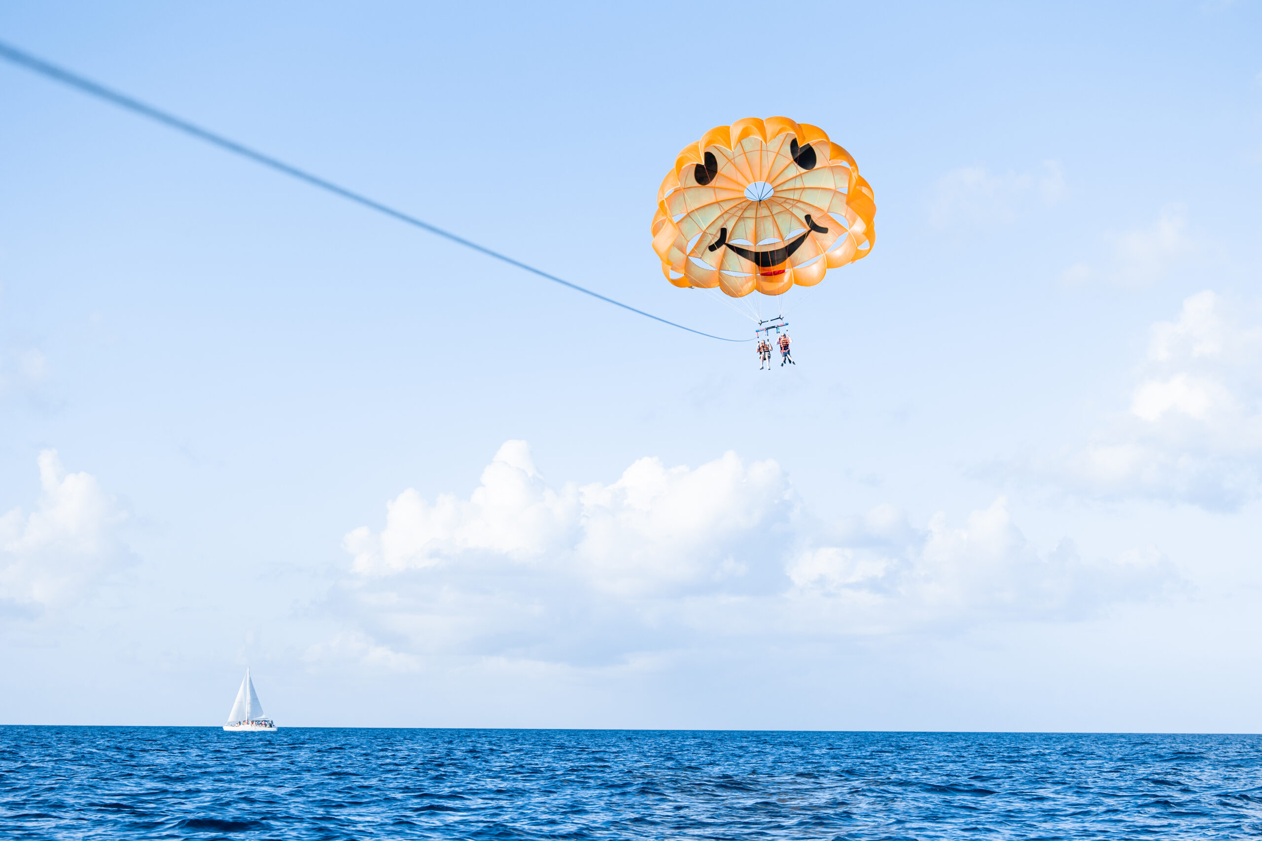 Two people on the Cozumel parasailing tour high above the water using a yellow parasail with a huge smily face on it