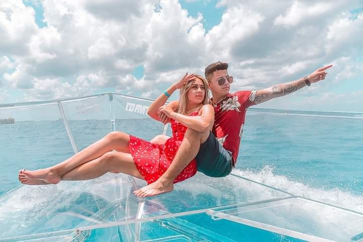 Two people, one male, one female, gazing off to the right while sitting on a clear perspex tour boat in beautiful blue caribbean waters. The man is pointing to something while the woman follws his gaze.