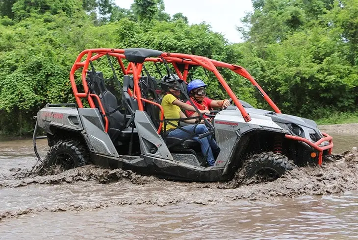 2 to 4 people with seatbelts, helmets and mouths protections are riding an Xrail car through the beautifully wild and muddy jungle road of Cozumel.