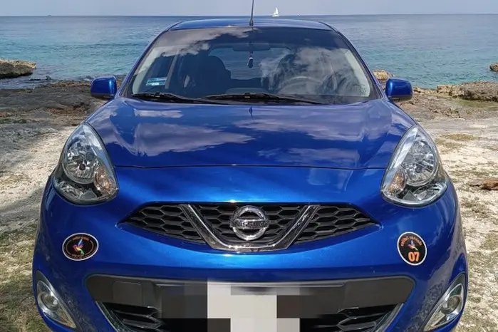 Photo of the front of a blue Nissan March Rental, with the wonderful Caribbean Sea in the background